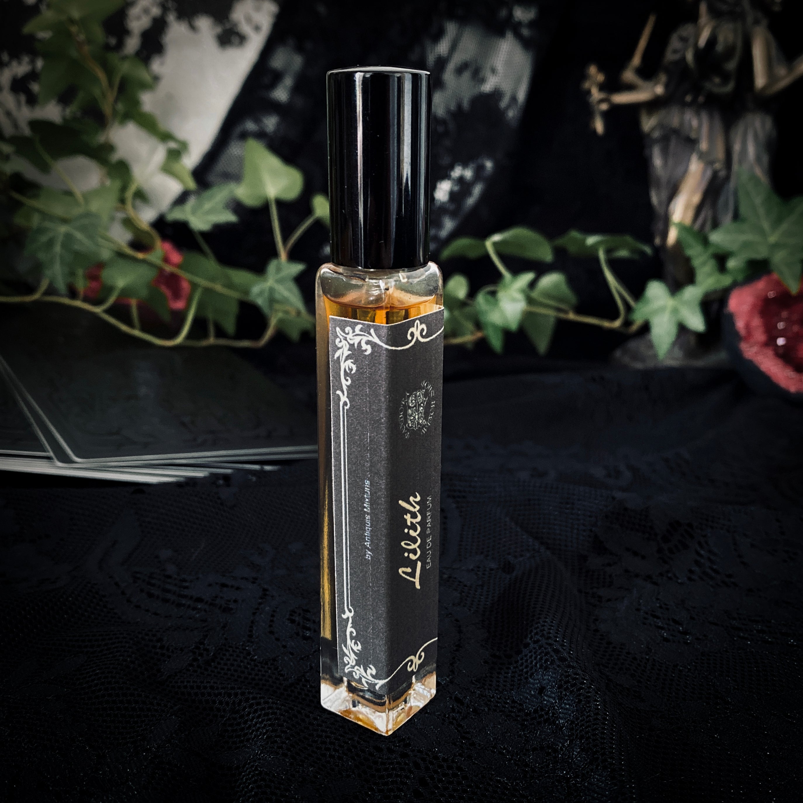 Three black glass bottles of ritual perfumes labeled Lilith, Witching Hour, and Hekate. Styled with dried flowers, candles, and witchcraft accessories on a dark mystical background. Product photo for a witch shop offering international shipping