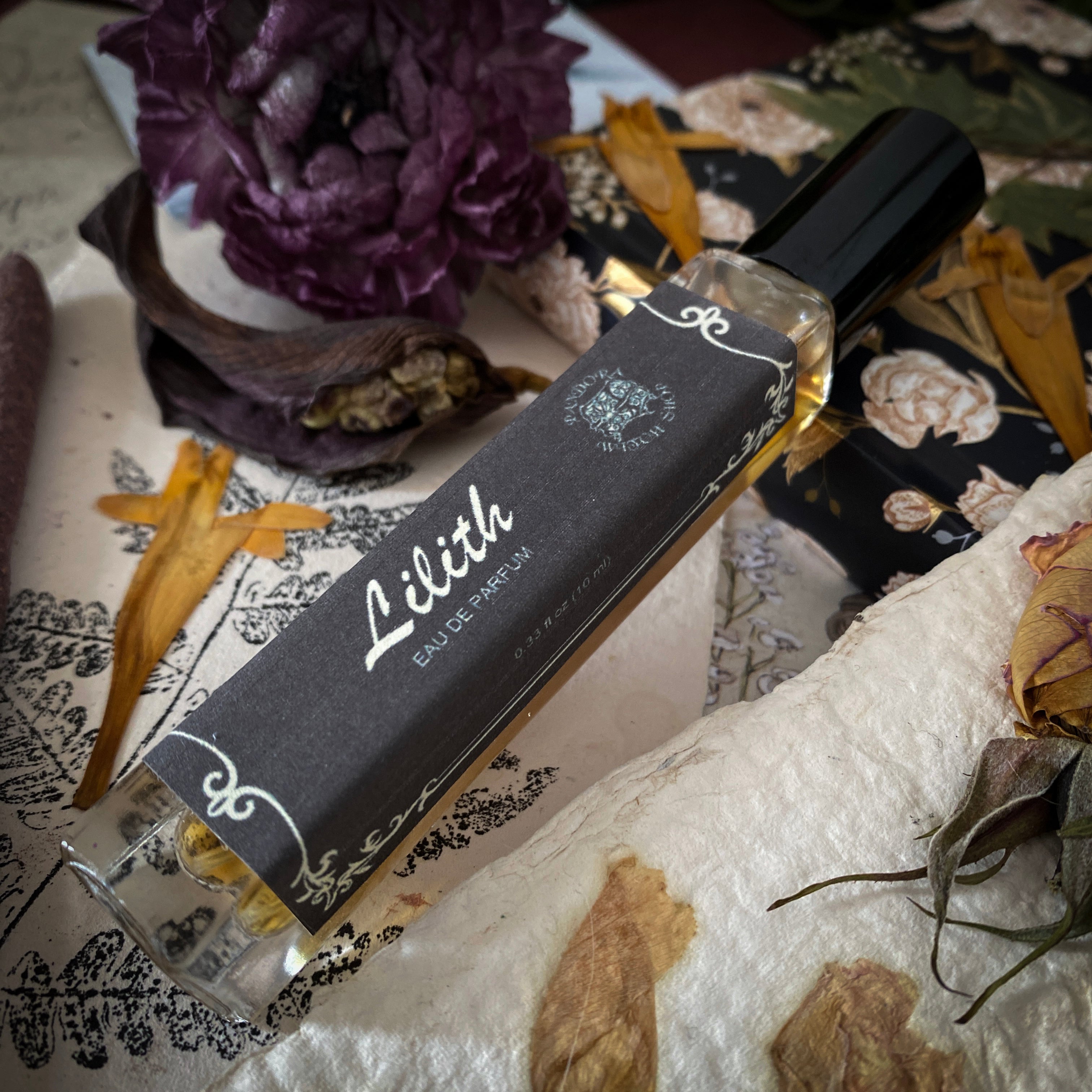 Perfume bottle labeled 'Lilith' on a decorative surface with flowers and ribbons.