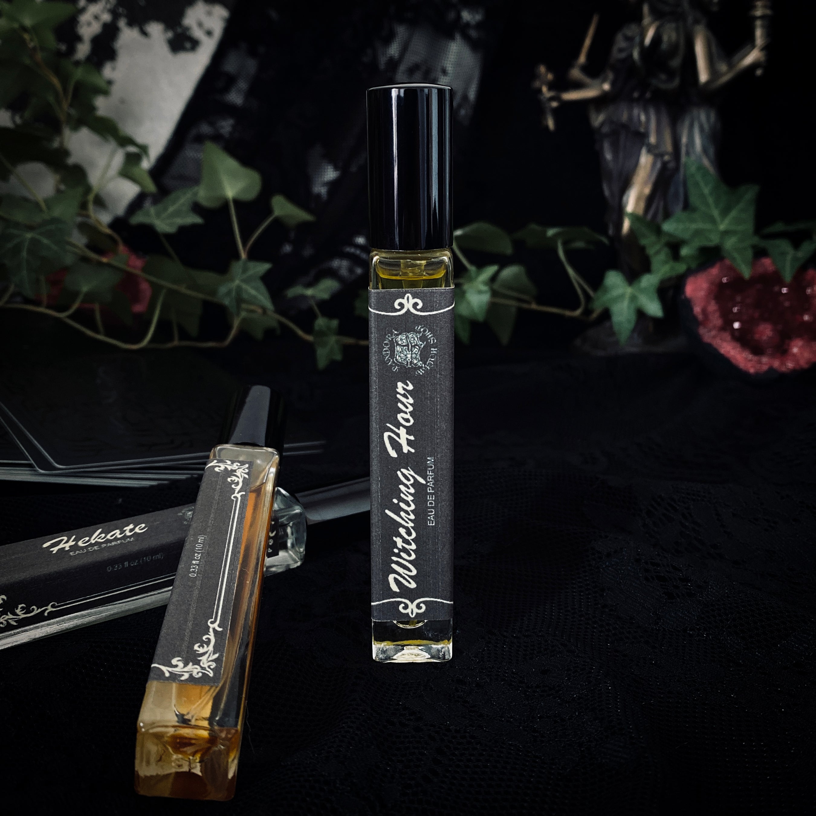 Three black glass bottles of ritual perfumes labeled Lilith, Witching Hour, and Hekate. Styled with dried flowers, candles, and witchcraft accessories on a dark mystical background. Product photo for a witch shop with international shipping