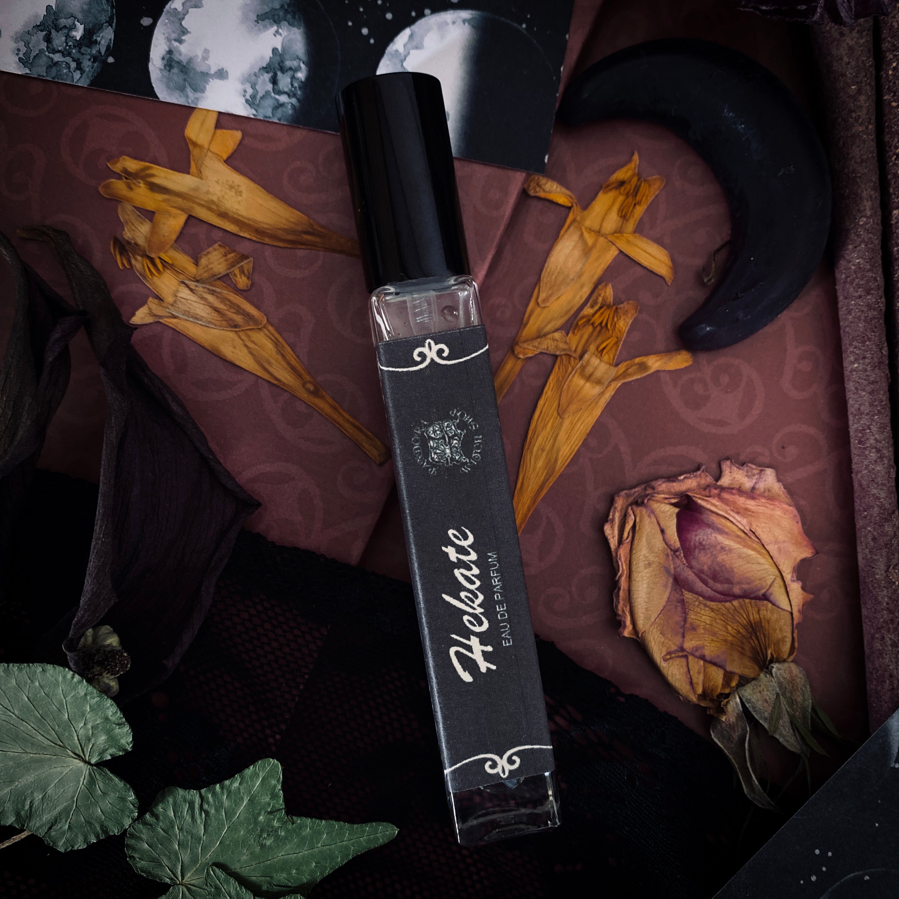 Perfume bottle labeled 'Hekate' on a mystical-themed background with dried flowers and moon symbols.