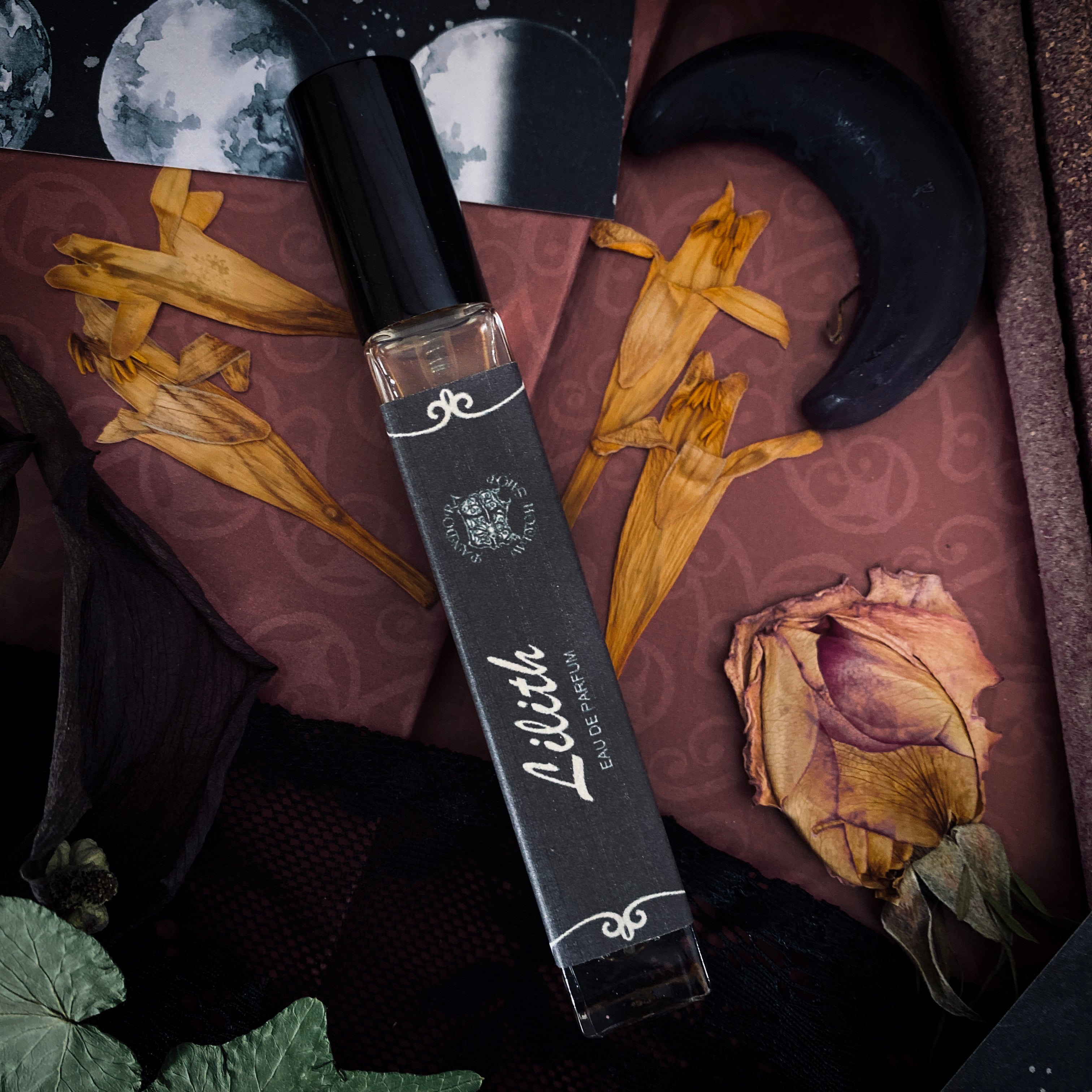 Perfume bottle labeled 'Lilith' on a decorative surface with dried flowers and a moon symbol.