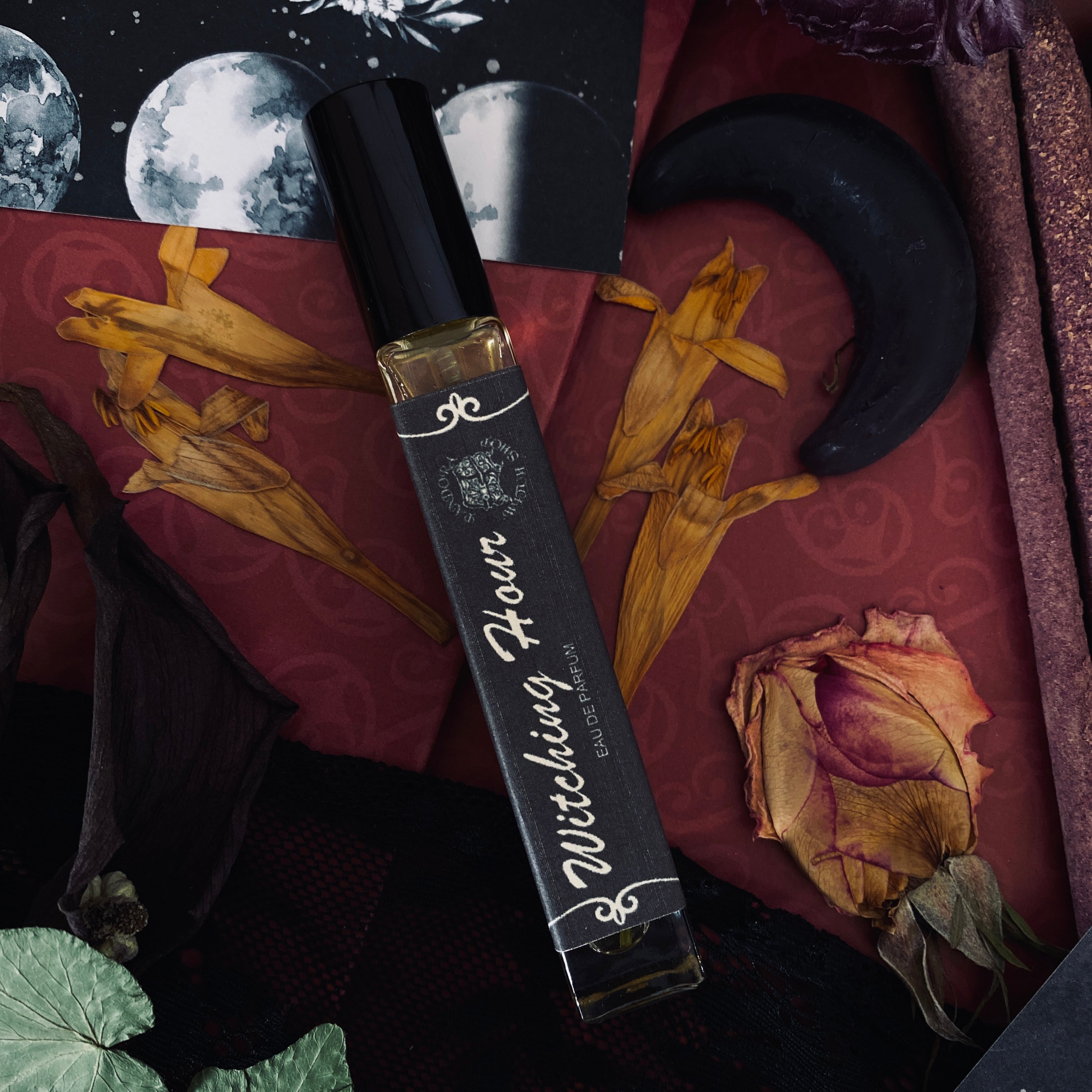 Three black glass bottles of ritual perfumes labeled Lilith, Witching Hour, and Hekate. Styled with dried flowers, candles, and witchcraft accessories on a dark mystical background. Product photo for a witch shop with international shipping