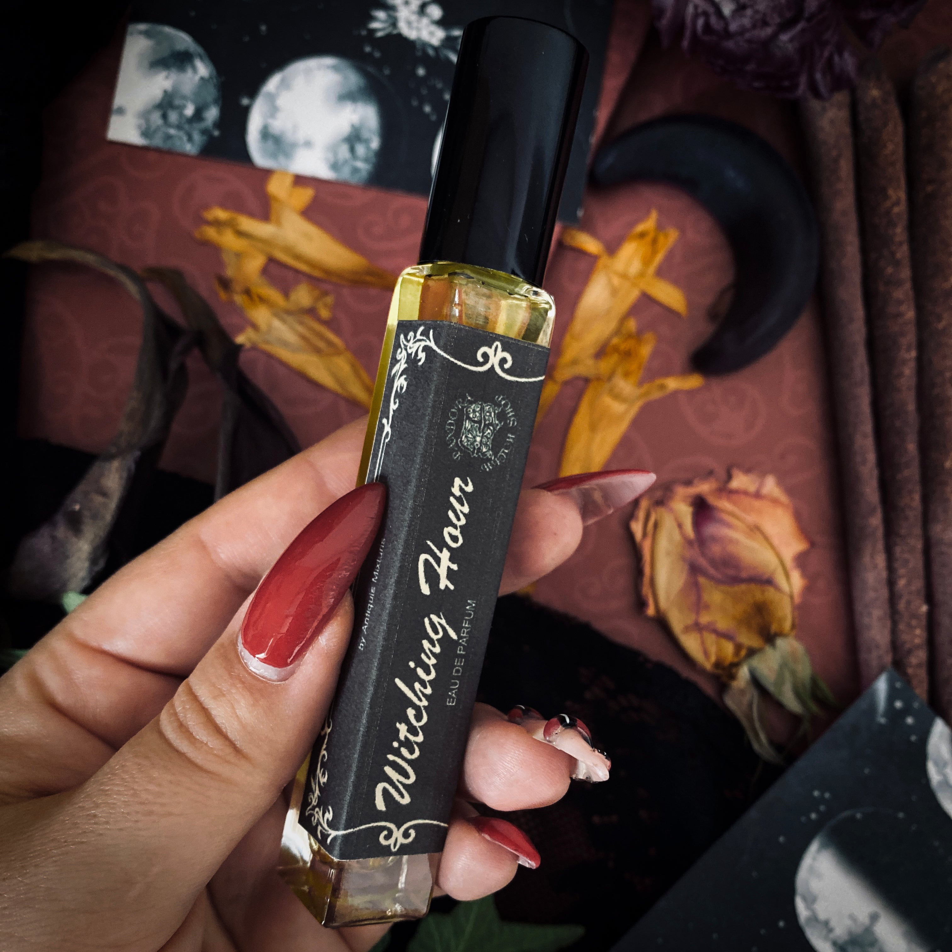 Hand holding a black and gold vape pen with 'Witching Hour' branding against a mystical background.
